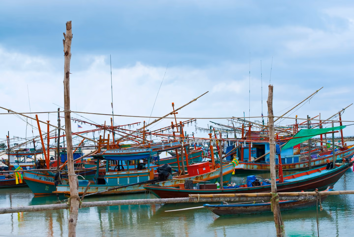 Painted wooden fishing boats with tall poles and lamp rigs moored close together in the harbour of Chaloklum