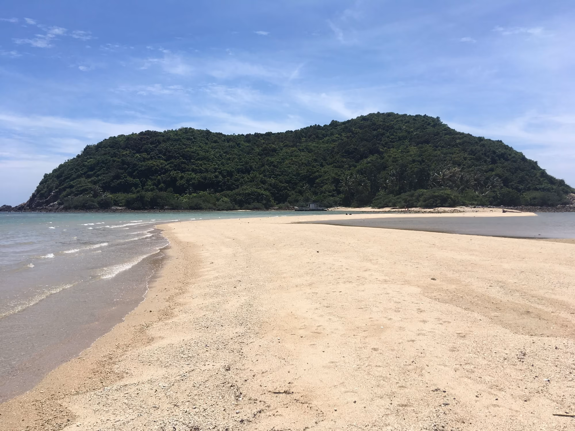 A sandbar of pale sand leading through shallow water to the forested islet of Ko Ma