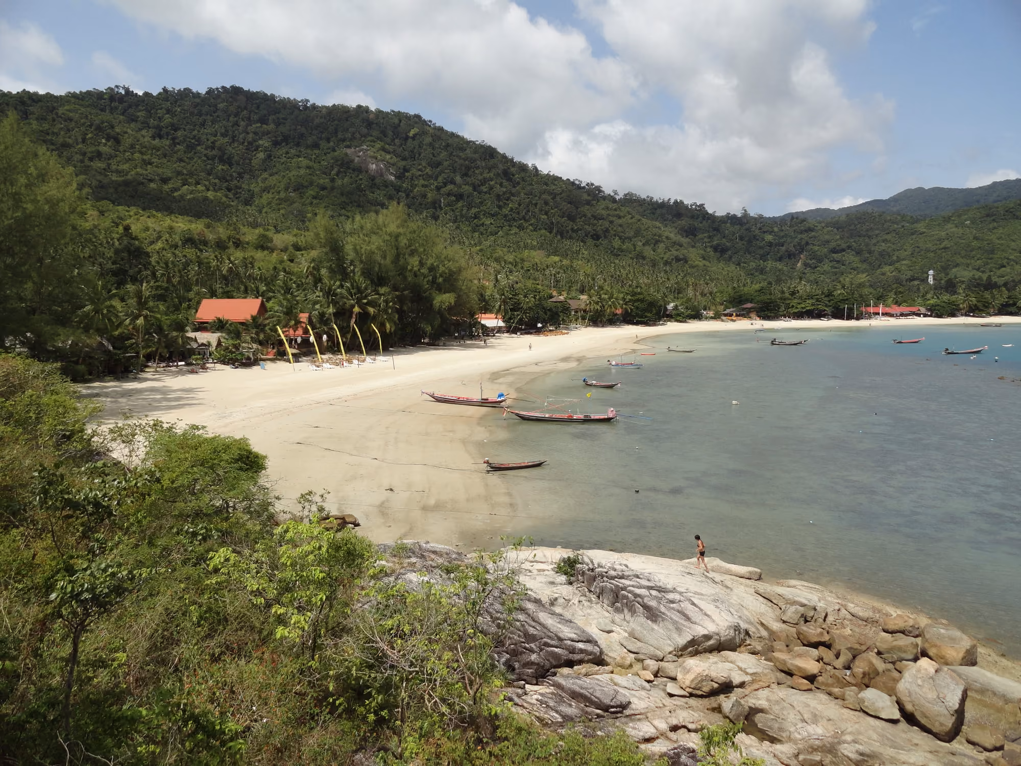 The curved sandy bay of Thong Nai Pan Yai seen from the granite rocks at one end of the beach, with longtail boats and jungle-covered hills
