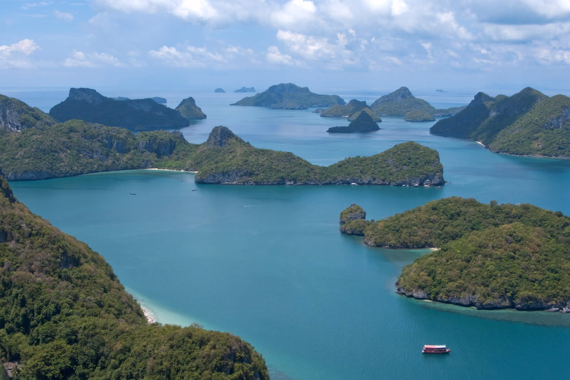Steep green limestone islands of Mu Ko Ang Thong in calm blue water, with a small boat crossing the channel