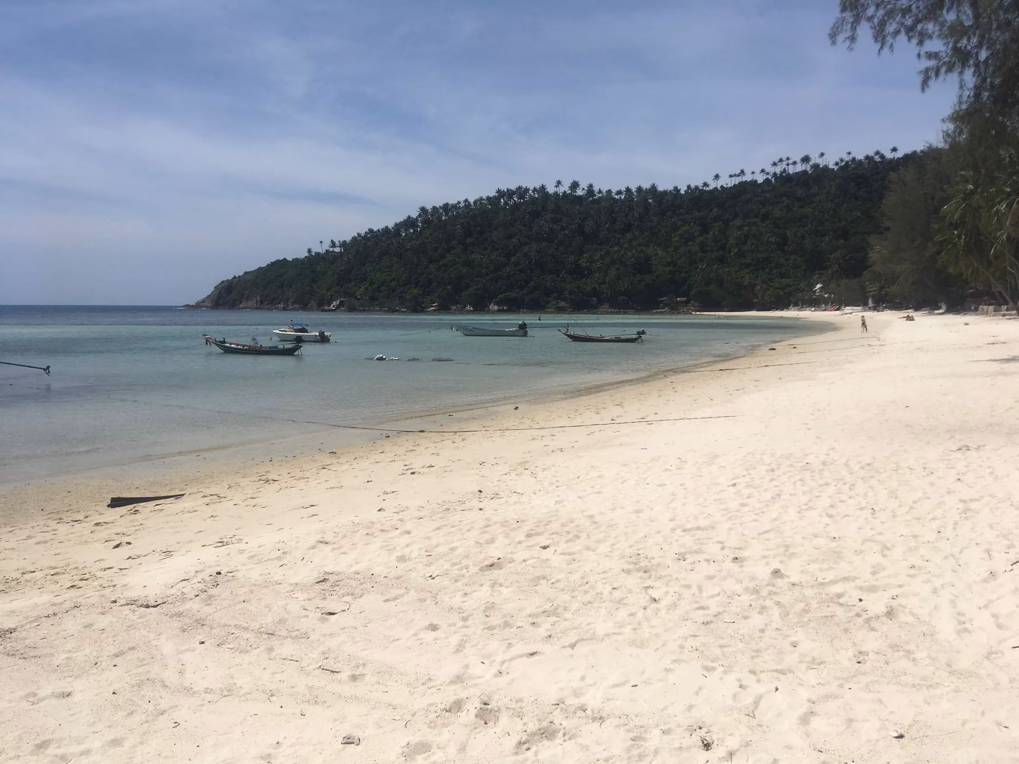Wide white sand at Haad Salad, a calm bay with a few longtail boats and a palm-covered headland