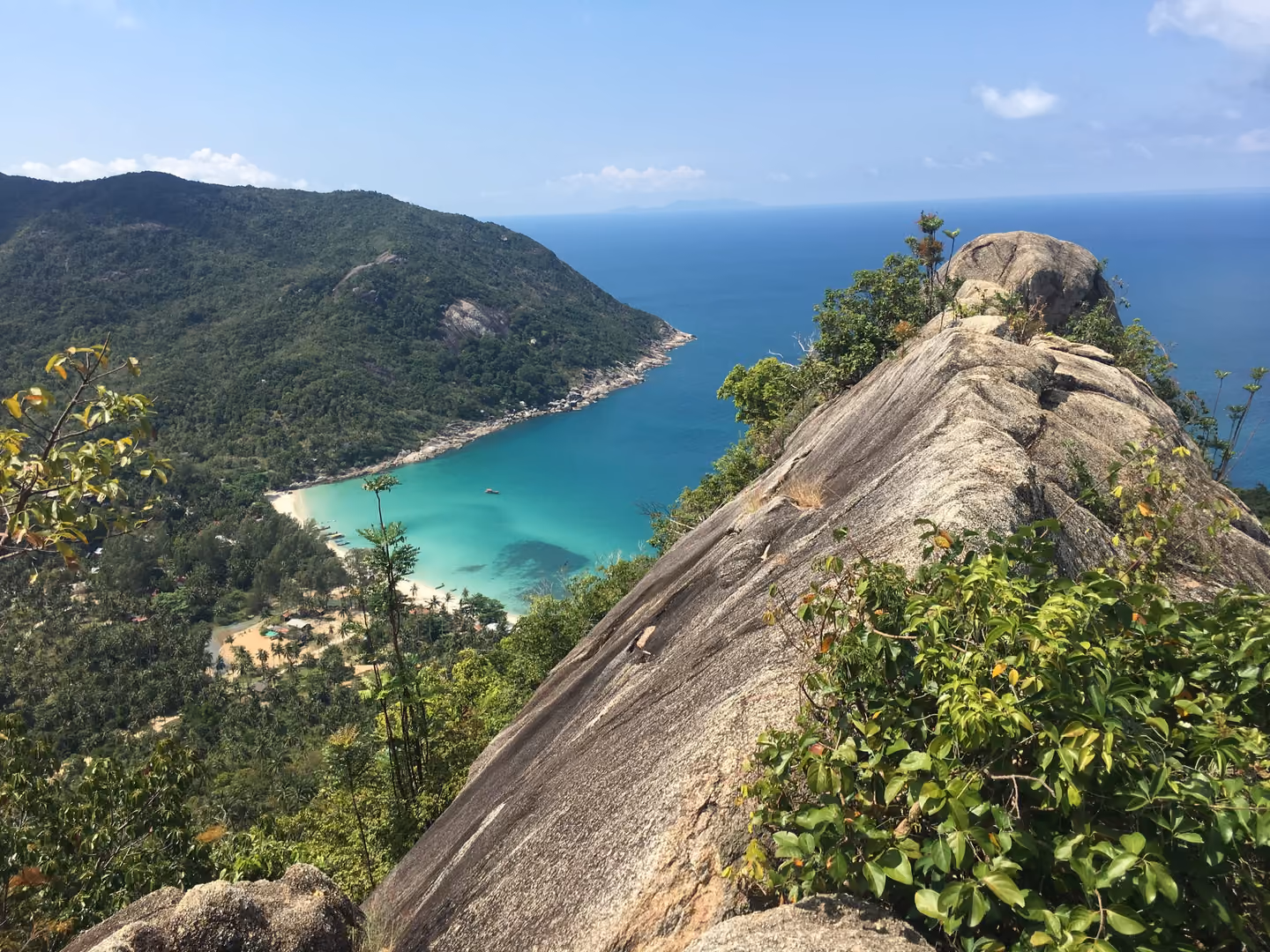 A bare granite ridge in the foreground and, far below, the turquoise bay of Bottle Beach framed by forested hills